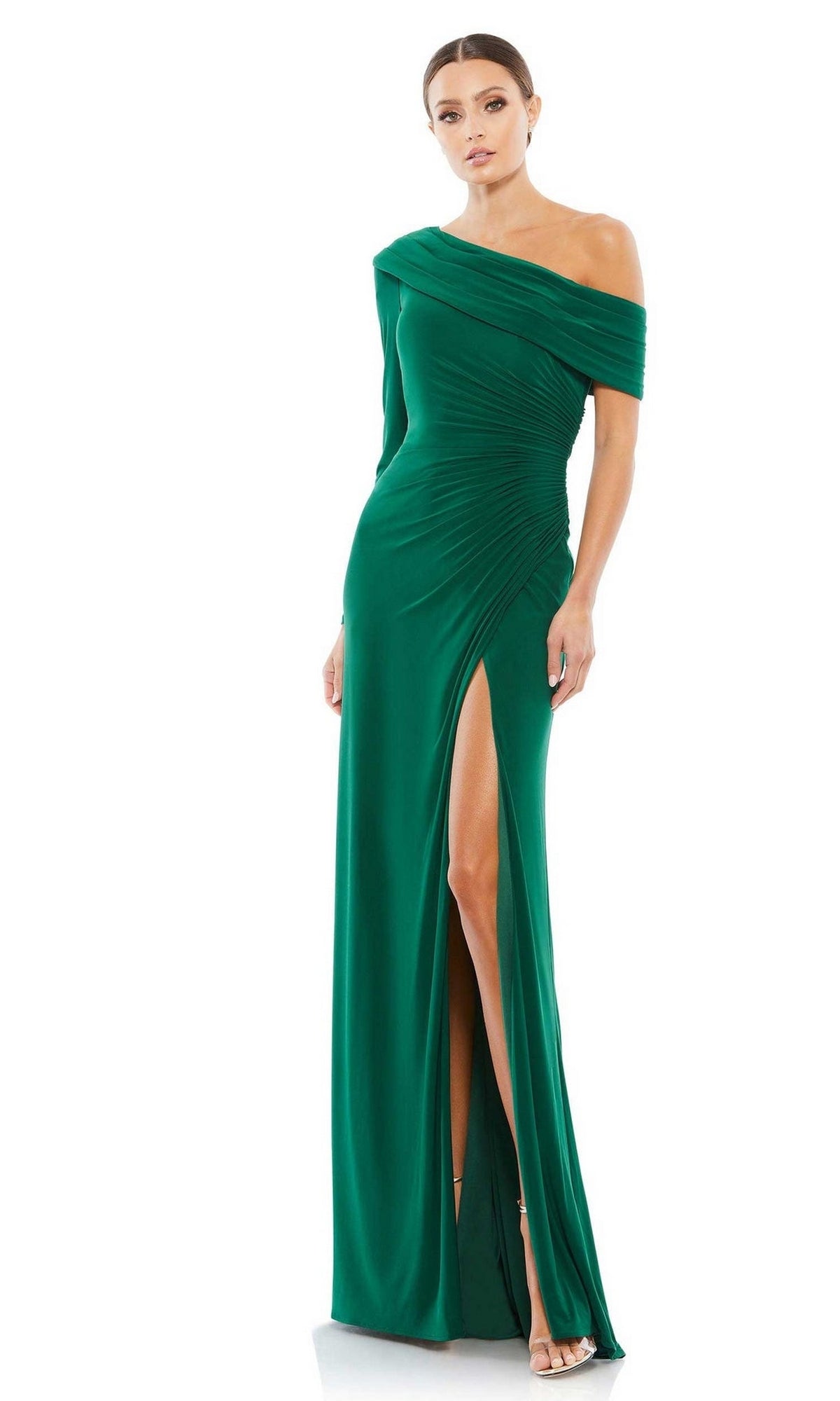 A woman models the Mac Duggal 26570 drop-shoulder long formal dress, featuring an elegant green hue and high slit, standing against a white background.